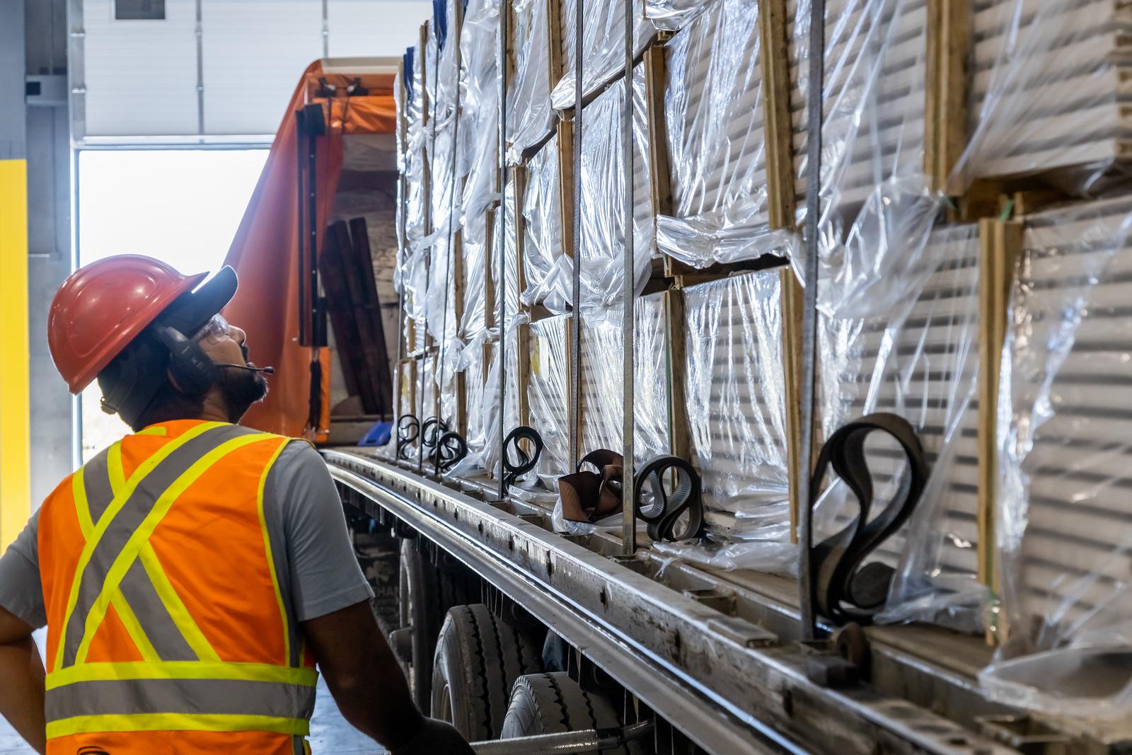 Man in hard hat inspecting skids of moulding on a delivery truck