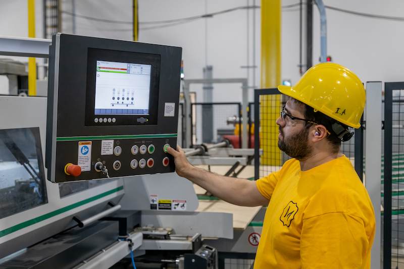 Metrie employee standing in front of a computer working the pre-finished moulding machine.