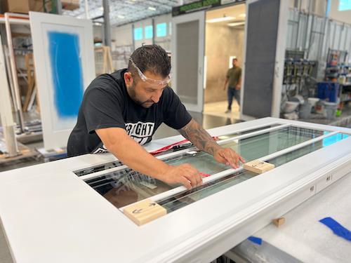 Empleado de Metrie midiendo el vidrio de una puerta exterior en el taller de puertas