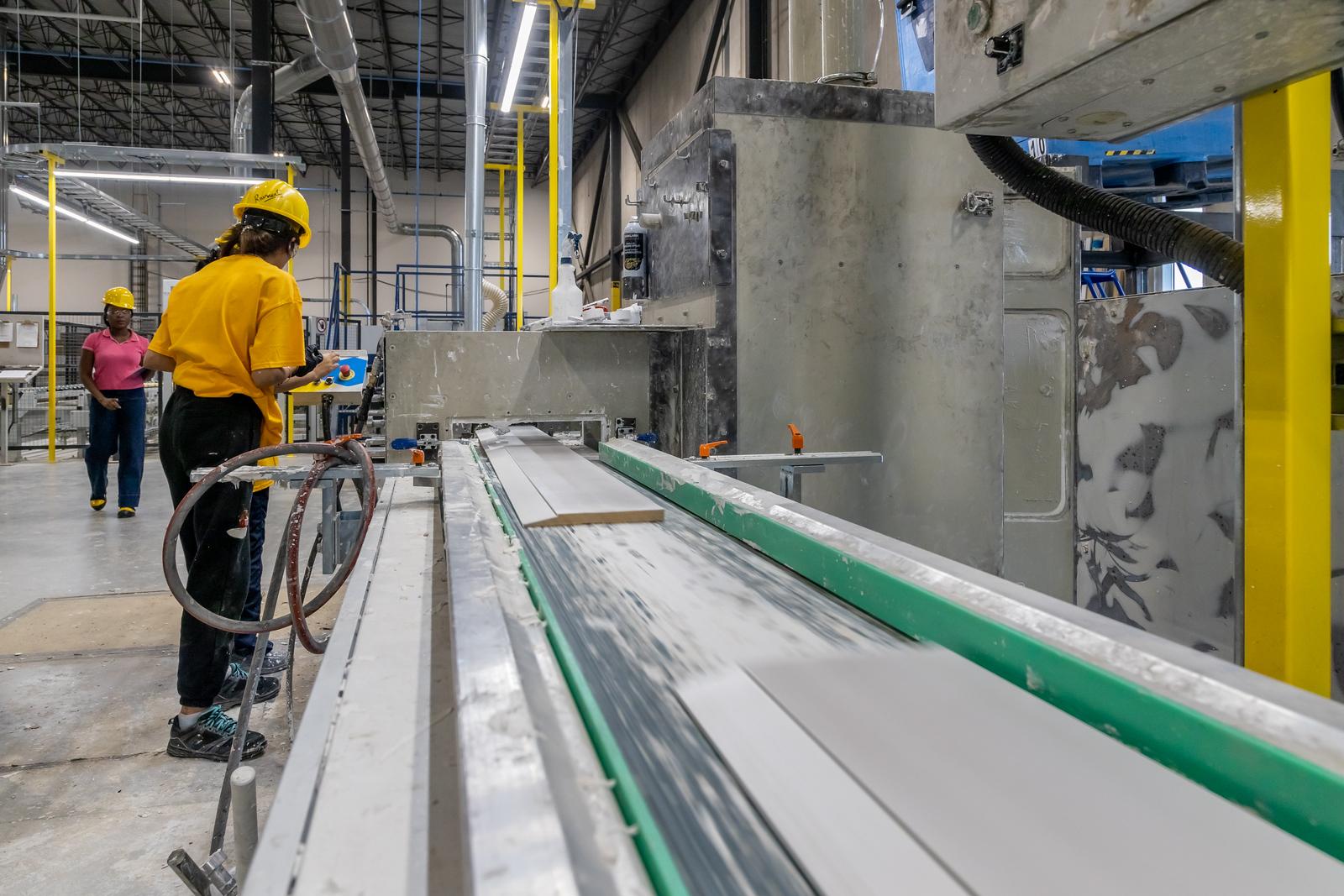 Woman in hard hard priming MDF baseboards in a manufacturing plant