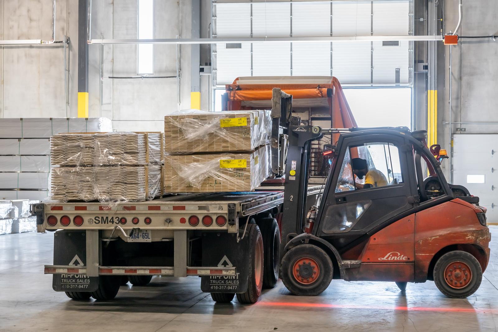 Forklift loading a pallet of primed MDF baseboards onto a flatbed truck