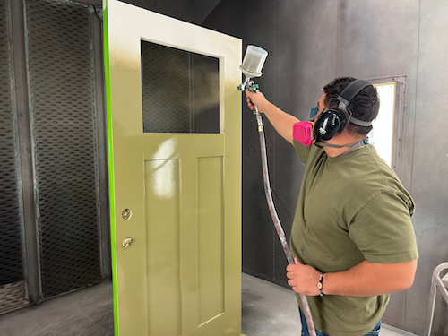 Empleado de Metrie pintando una puerta exterior de color verde musgo con un pulverizador de pintura